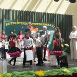 Grupa dorosłych i dzieci na scenie podczas rozdawania upominków.