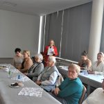 Grupa starszych pań na sali konferencyjnej. Jedna z nich przemawia za pomocą mikrofonu.