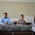 Mężczyzna w błękitnej koszuli oraz dwie kobiety siedzący przy podłużnym stole.