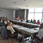 Grupa osób starszych i niepełnosprawnych w sali konferencyjnej urzędu miejskiego