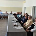 Grupa osób starszych w sali konferencyjnej urzędu miejskiego. W najdalszej częsci planu siedzą mężczyzna w jasnej koszuli i dwie młode kobiety.