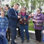 Męzczyzna w garniturze przekazuje starszej kobiecie listę do podpisania. Na około kobiety z dziećmi.