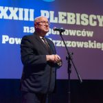 Starszy mężczyznaw garniturze przemawia do mikrofonu.