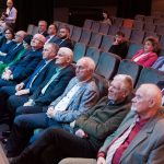 Grupa osób dorosłych osób w odswiętnych strojach siędzacych na sali kinowej.