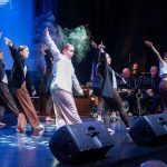 Grpa dziewcząt tańczacych na scenie sali kinowej.