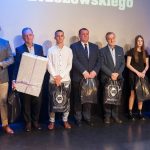 Grupa mężczyzn i kobiet pozujacych do zdjęcia. Prawie wszyscy trzymają podarki.