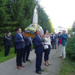 Ludzie elegancko ubrani, 4 osoby trzymają figurkę Matki Boskiej