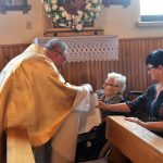 Mężczyzna pochyla się nad kobietą. Obok siedzi druga kobieta a w tle mężczyzna z telefonem robi zdjęcie.