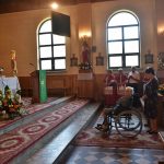 Kobieta na wózku inwalidzkim wraz z ludźmi modlącymi się przed ołtarzem.