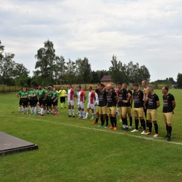 Grupa mężczyzn ubranych w stroje piłkraskie stoi na murawie boiska.