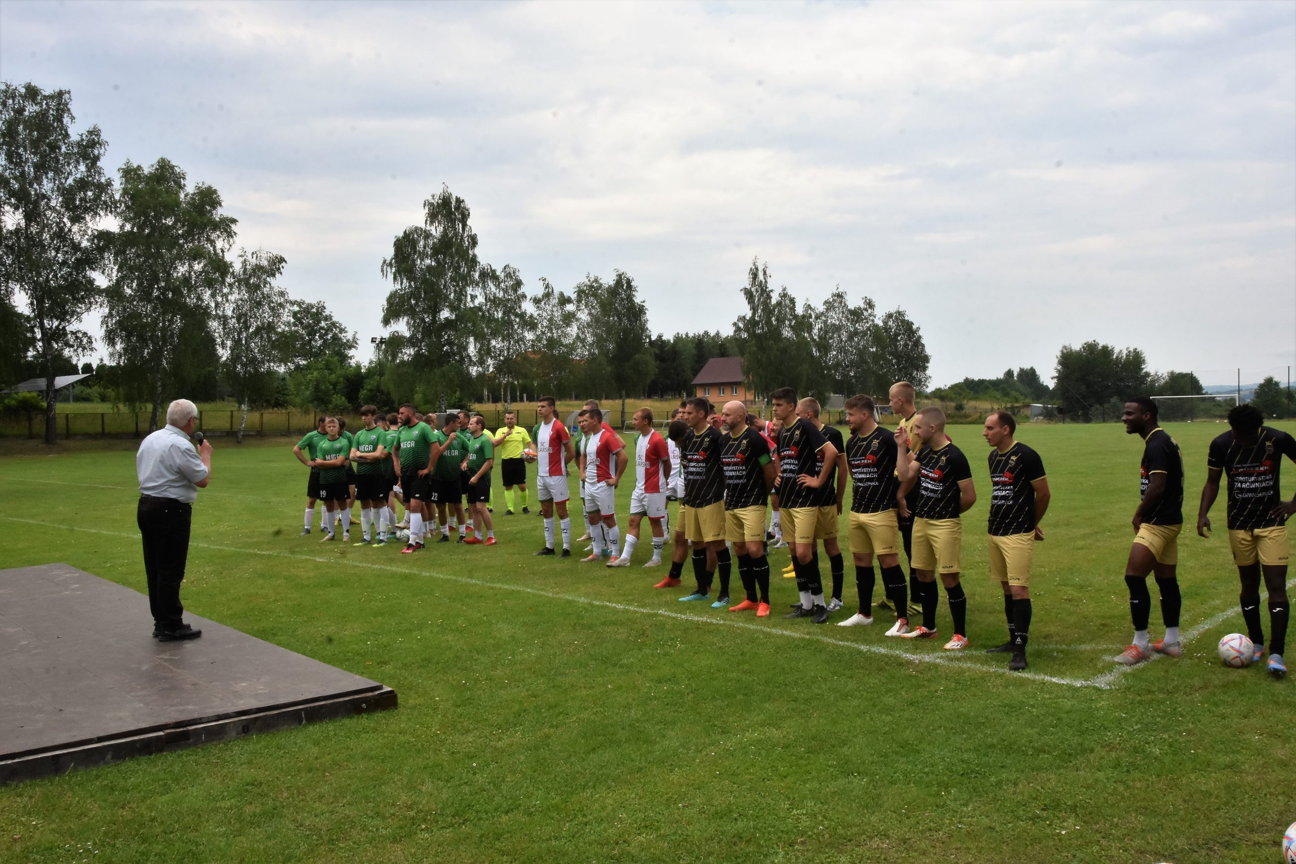 Grupa mężczyzn ubranych w stroje piłkraskie stoi na murawie boiska.