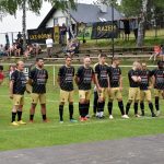 Grupa mężczyzn ubrani w sportowe stroje, stoją na murawie.