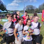 Grupa dzieci chłopców i dziewcząt uśmiechnięty stoi na boisku sportowym.