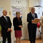 Grupa osób dwie kobiety i dwóch mężczyzn stoją w jasnej sali i przemawiają do dzieci.