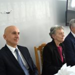 Grupa trzech osób starszych siedzi przy stole i ogląda występ.