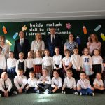 Grupa dzieci stoi na sali i pzouje do wspólnego zdjęcia. za nimi stoją kobiety i dwóch mężczyzn.