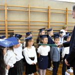 Starszy mężczyzna w garniturze przykłada na ramię dziewczyczynce duży ołówek i pasuje na ucznia.