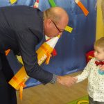 Starszy mężczyzna w gafrniturze pasuje zółtym ołowkiem chłopca na przedszkolaka