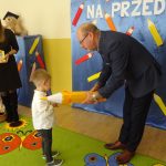 Starszy mężczyzna w gafrniturze pasuje zółtym ołowkiem chłopca na przedszkolaka