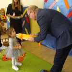 Starszy mężczyzna w gafrniturze pasuje zółtym ołowkiem dziewczynkę na przedszkolaka