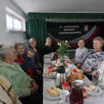 Grupa starszych kobiet siedzi przy stole swiatecznym i smieją się do siebie.