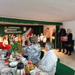 Grupa starszych kobiet siedzi przy stole swiatecznym i smieją się do siebie oraz ogladają występ dzieci.