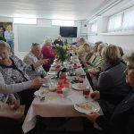 Grupa starszych kobiet siedzi przy stole swiatecznym i smieją się do siebie.