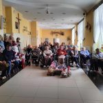 Wspólne zdjęcie osób starszych na wóxkach inwaldzkich w jasnej sali.