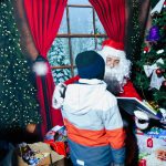 Młody chłopak odbiera od swietego mikołaja prezent. za nimi stoi choinka o tło bajkowe.