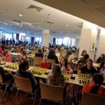 Grupa dzieci siedzi przy stole z tablicami szachowej i grają w karty.