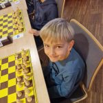 Chłopiec siedzi za stołem na którym są ułożone szachy.