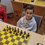 Chłopiec siedzi za stołem na którym są ułożone szachy.