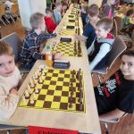 Grupa dzieci siedzi za stołem na którym są ułożone szachy.