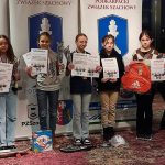 Grupa dzieci stoi na podium z dyplomami i medalami.