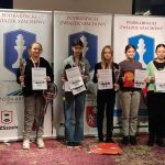 Grupa dzieci stoi na podium z dyplomami i medalami.