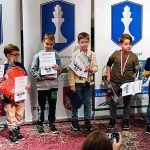 Grupa dzieci stoi na podium z dyplomami i medalami.