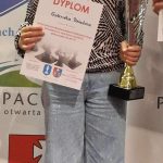 Dziwczynka stoi na podium z dyplomem, medalem i pucharem.