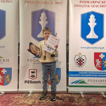 Chłopiec stoi na podium z dyplomem, medalem i pucharem.