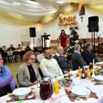 Grupa kobiet i mężczyzn ubranch w odświetne stroje siedzi przy swiatecznym stole.