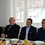 Czterech mężczzyn ubranych w garnitury siedzi przy świątecznym, wyłozonym bialym obrusem stole w jasnej sali.