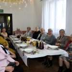 Grupa starszych kobiet ubranch w odświetne stroje siedzi przy swiatecznym stole.