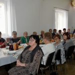 Grupa starszych kobiet ubranch w odświetne stroje siedzi przy swiatecznym stole.