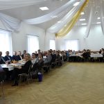 Grupa osób mężczyzn i kobiet siedzą w sali domu ludowego przy świątecznym stole.