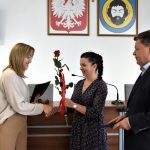 Kobieta o ciemnych włosach przekazuje kobiecie o blond włosach rózyczkę.