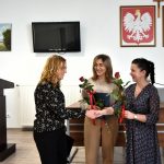 Kobieta o ciemnych włosach przekazuje kobiecie o blond włosach rózyczkę.