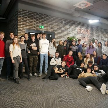 Grupa młodych osób stoi w pomieszczeniu, w odcieniach brązu i pozują do grupowego zdjęcia.