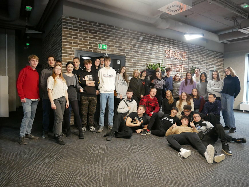 Grupa młodych osób stoi w pomieszczeniu, w odcieniach brązu i pozują do grupowego zdjęcia.