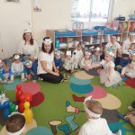 Grupa dzieci bawi się na kolorowym dywanie w przedszkolu.