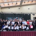 Grupa osób stoi na scenie, trzymając w rękach dyplomy i pozuje do grupowego zdjęcia.