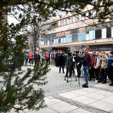 Grupa młodzieży stoi na placu przed urzędem w centrum miasta.